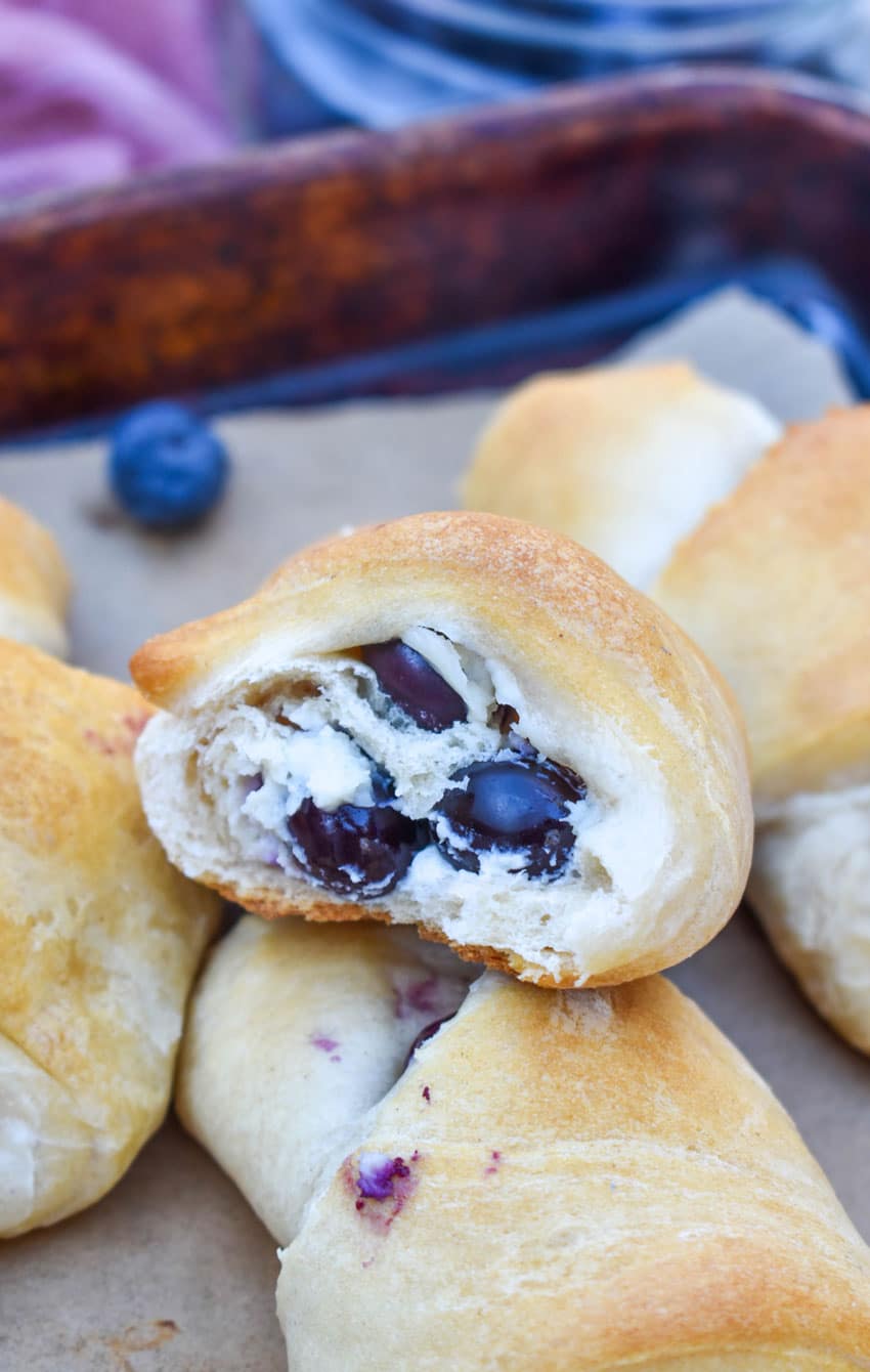 a bitten blueberry cream cheese crescent roll resting on top of another breakfast roll