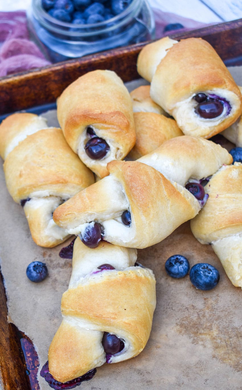 a pile of blueberry cream cheese crescent rolls on a parchment paper lined baking sheet