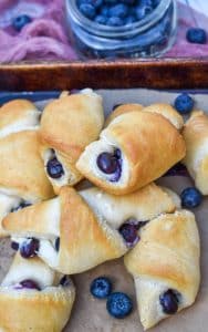 a pile of blueberry cream cheese crescent rolls on a parchment paper lined baking sheet