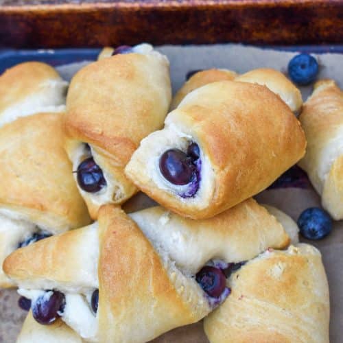 a pile of blueberry cream cheese crescent rolls on a parchment paper lined baking sheet