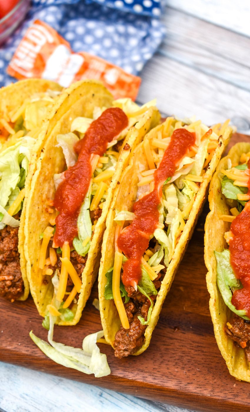 copycat taco bell mild sauce on beef tacos arranged in a row on a wooding cutting board