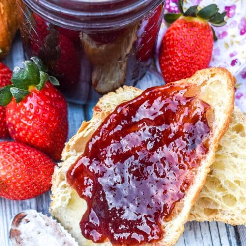 a strawberry jam recipe without pectin spread on a halved croissant roll surrounded by fresh strawberries