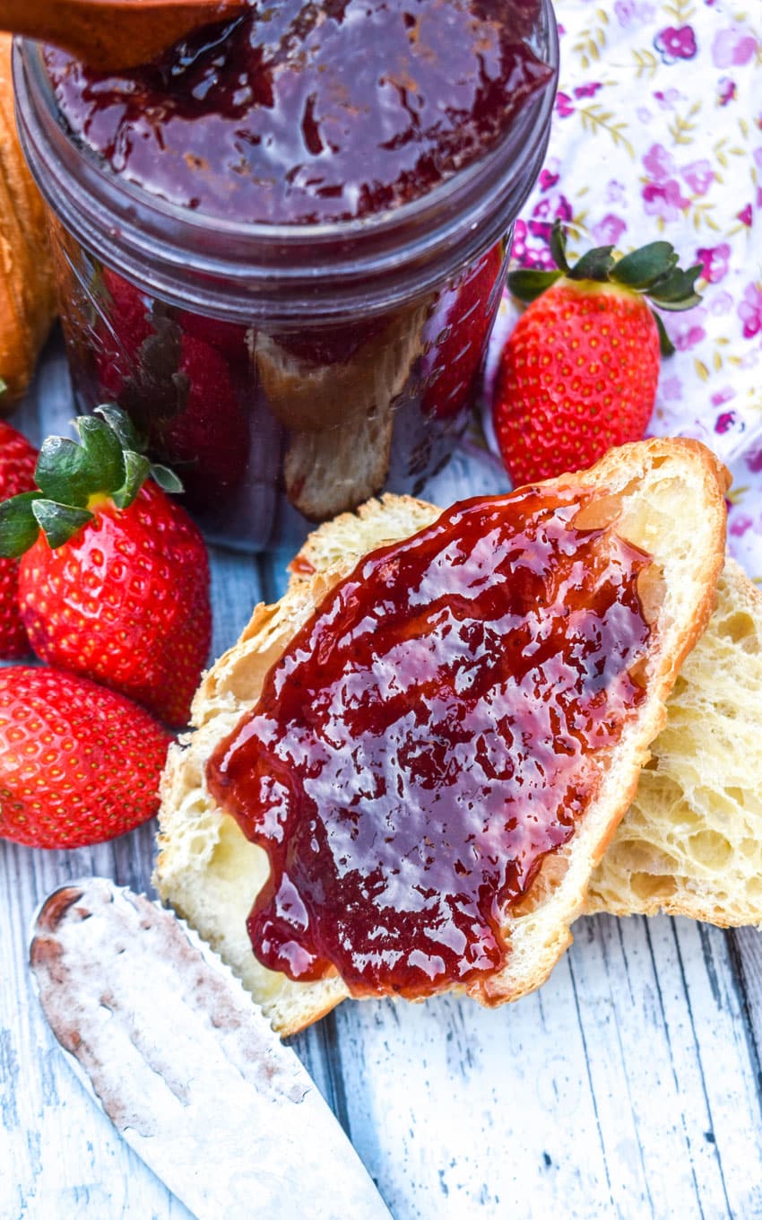 a strawberry jam recipe without pectin spread on a halved croissant roll surrounded by fresh strawberries