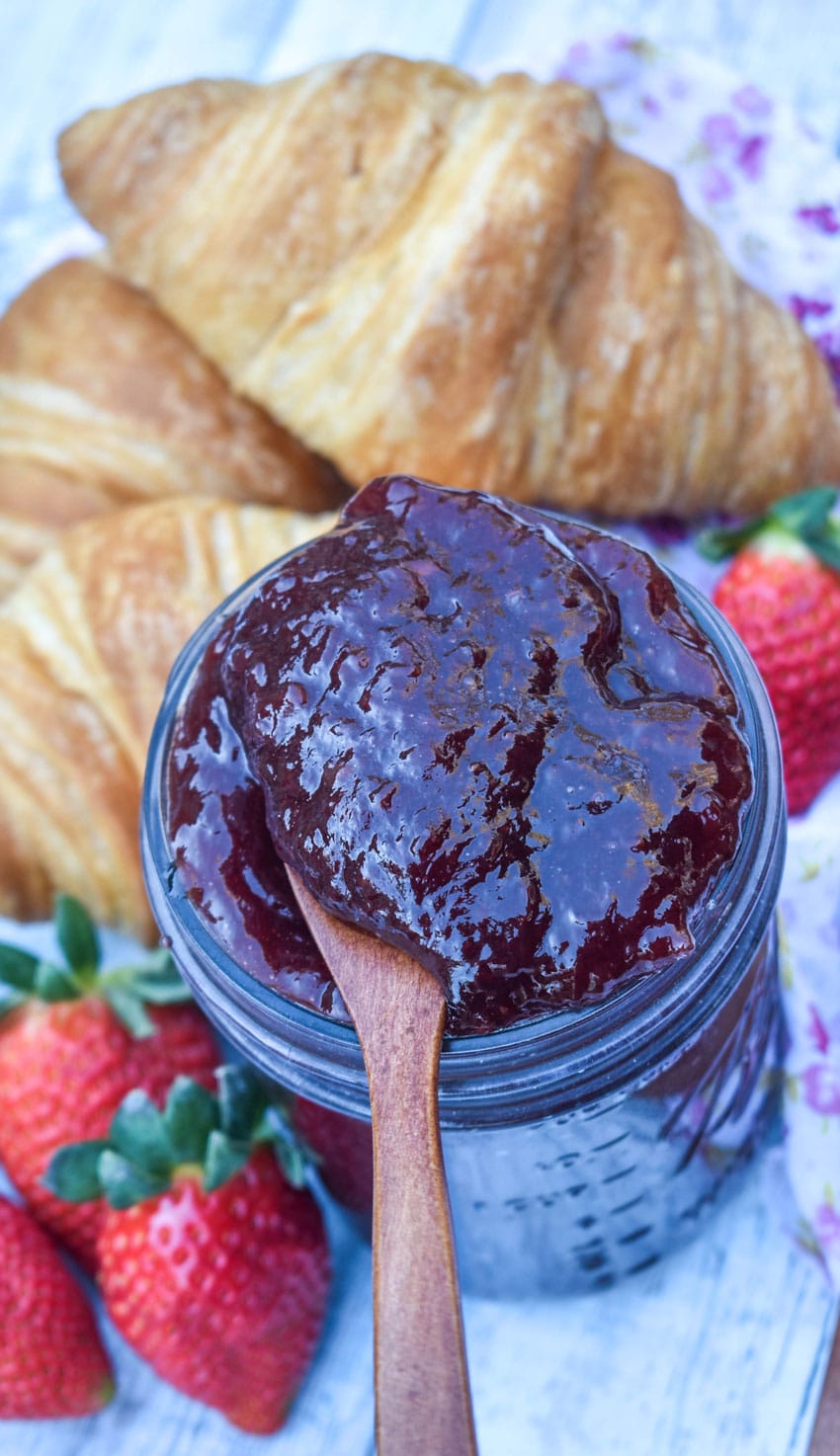 a wooden spoon scooping easy strawberry jam out of a glass jar