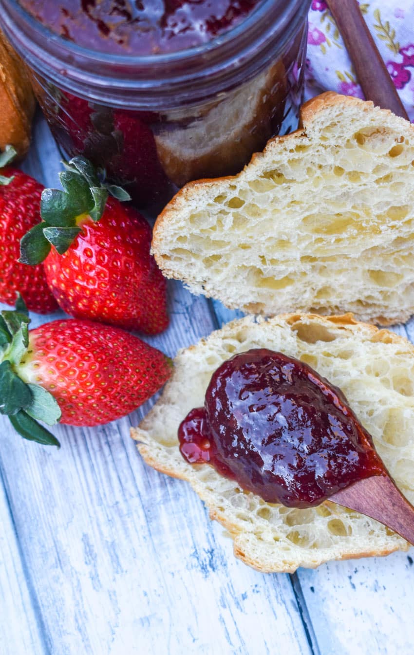 a wooden spoon holding a scoop of easy strawberry jam resting on a halved croissant roll