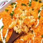 a wooden spoon scooping cheesy nashville hot chicken casserole out of a white baking dish