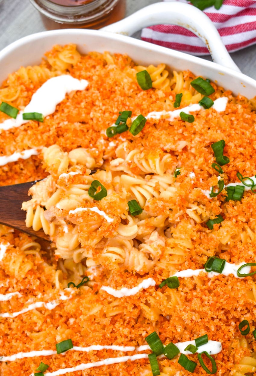 a wooden spoon scooping cheesy nashville hot chicken casserole out of a white baking dish