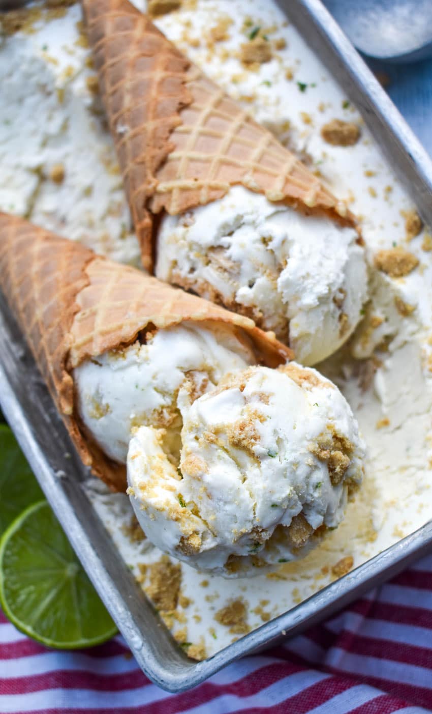 scoops of no churn key lime pie ice cream in waffle cones resting on top of a pan of ice cream