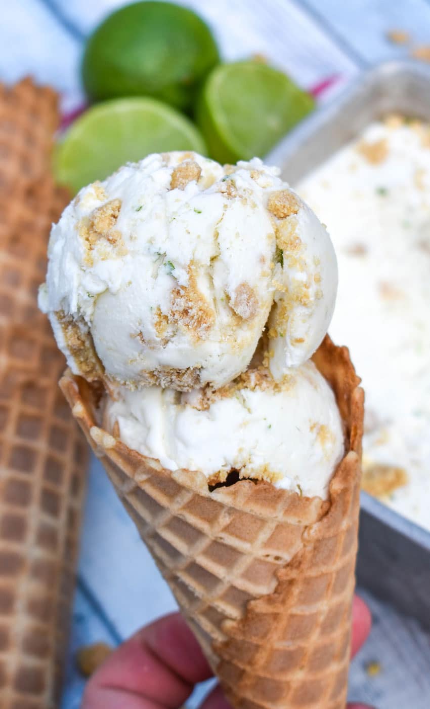 a hand holding up a waffle cone filled with scoops of no churn key lime pie ice cream