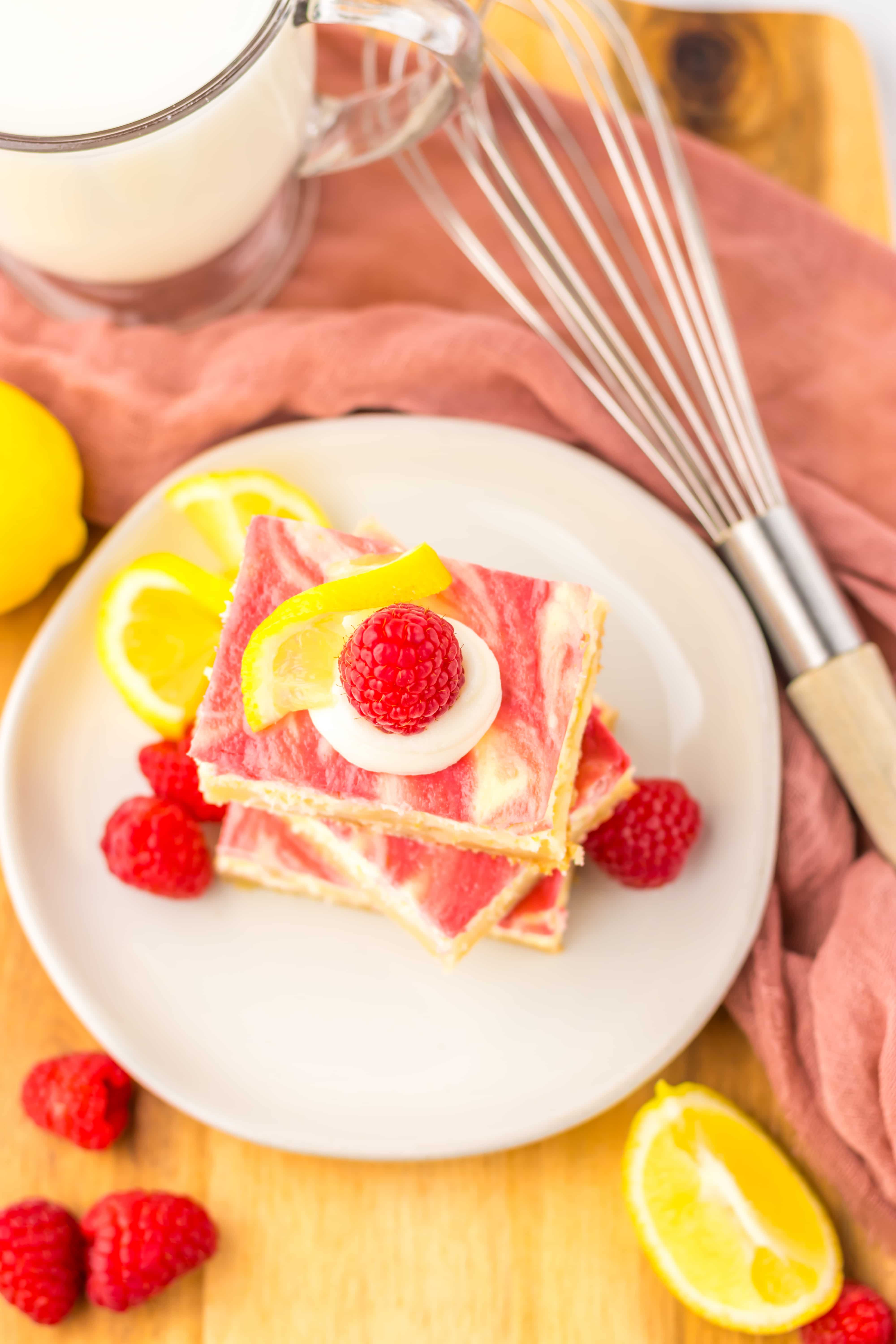 three raspberry lemon cheesecake bars stacked on a white plate with fresh raspberries 