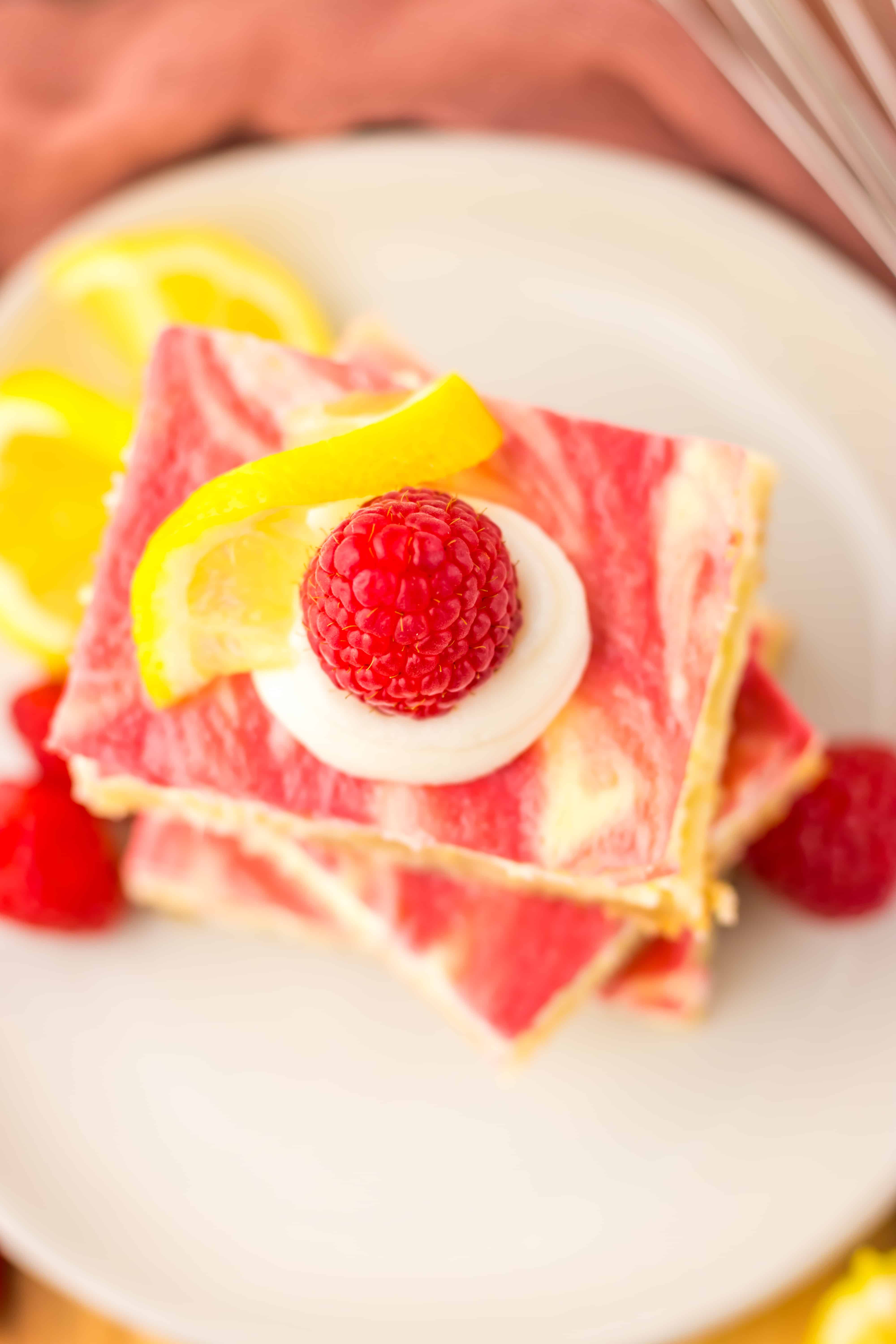 three raspberry lemon cheesecake bars stacked on a white plate with fresh raspberries 