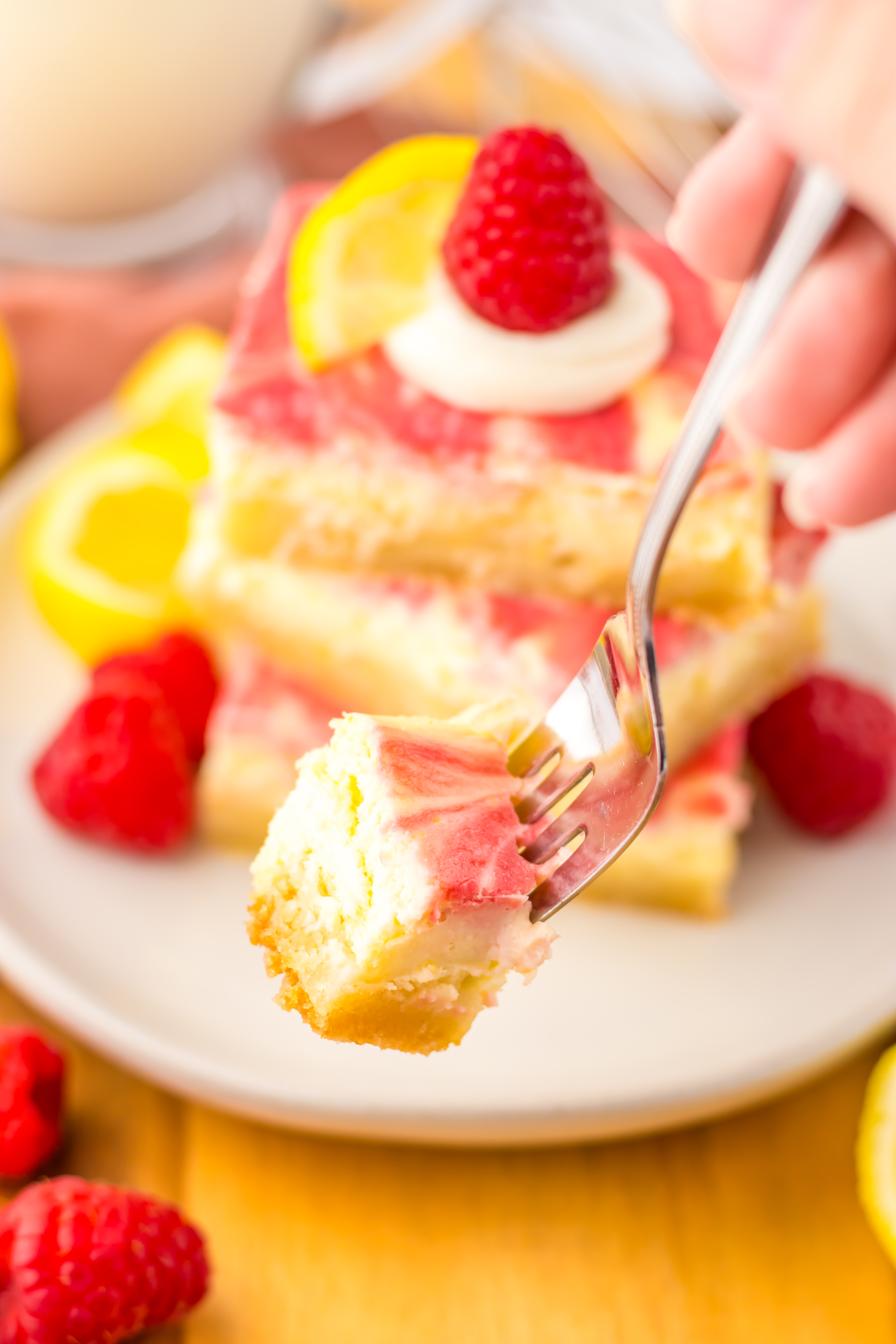 a silver fork holding up a bite of a raspberry lemon cheesecake bar