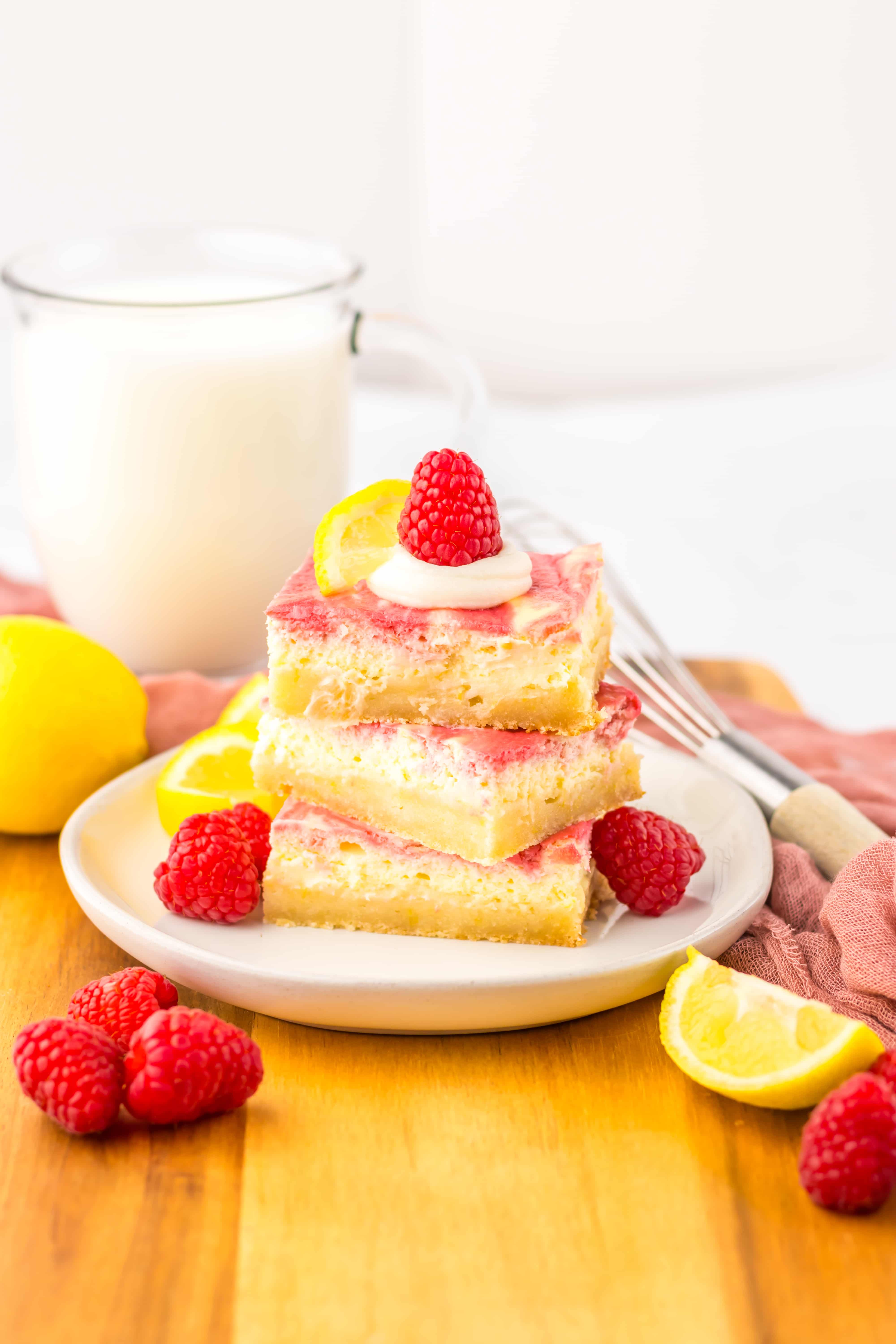 three raspberry lemon cheesecake bars stacked on a white plate with fresh raspberries 