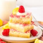 three raspberry lemon cheesecake bars stacked on a white plate with fresh raspberries