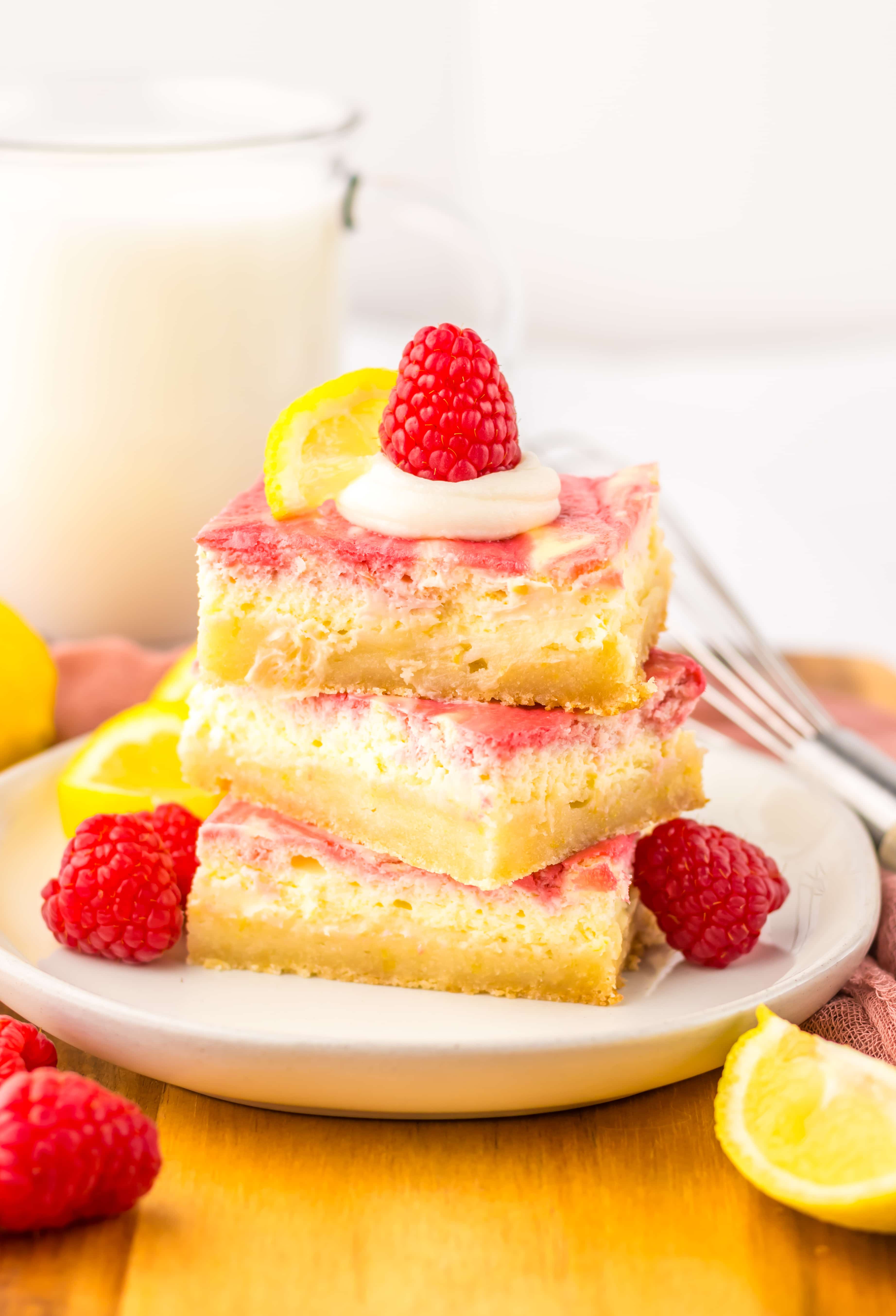 three raspberry lemon cheesecake bars stacked on a white plate with fresh raspberries 