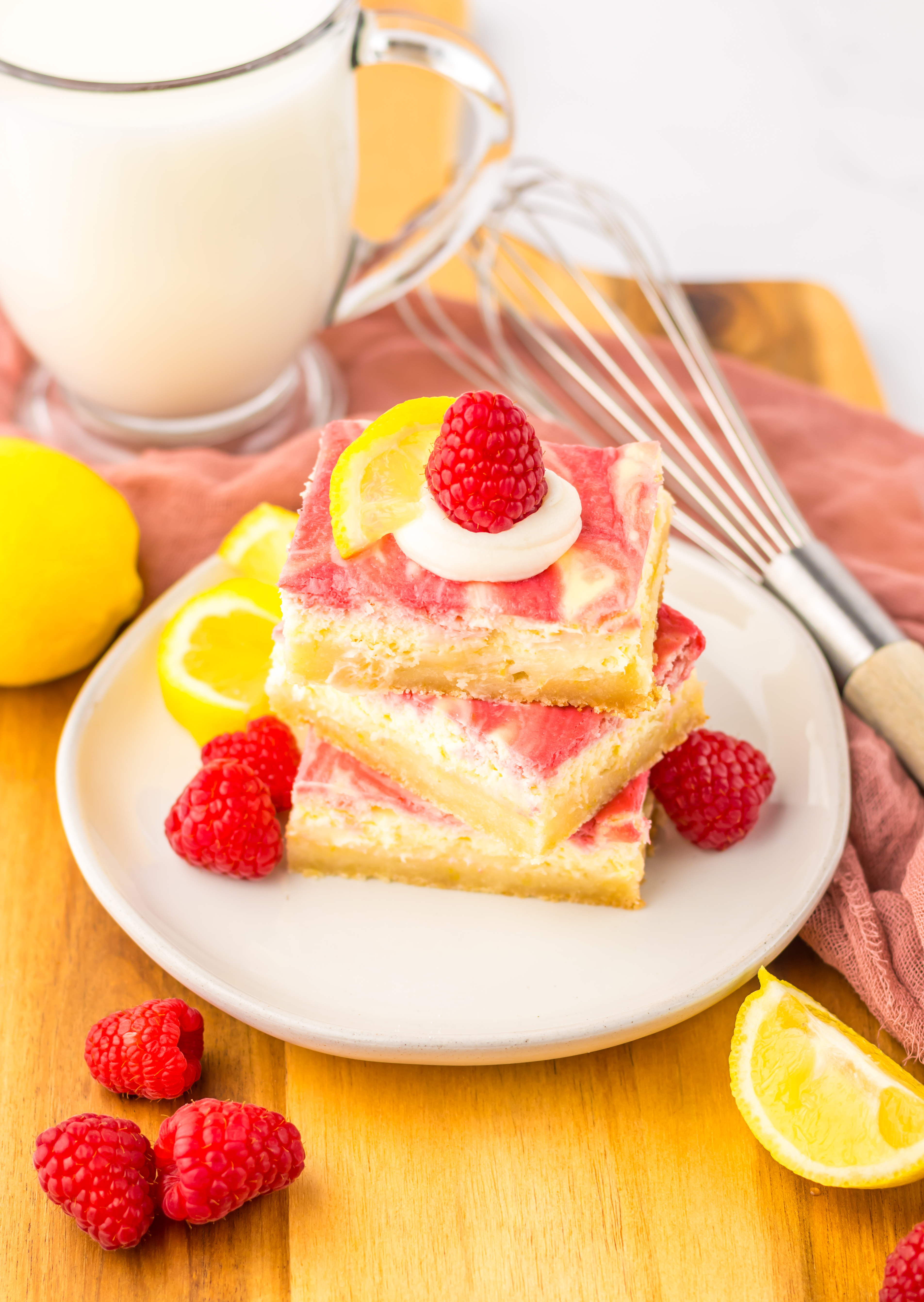 three raspberry lemon cheesecake bars stacked on a white plate with fresh raspberries 