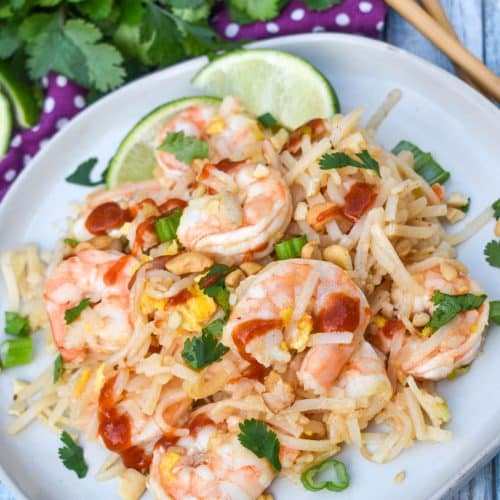 shrimp pad thai on a white plate with cilantro and chop sticks in the background