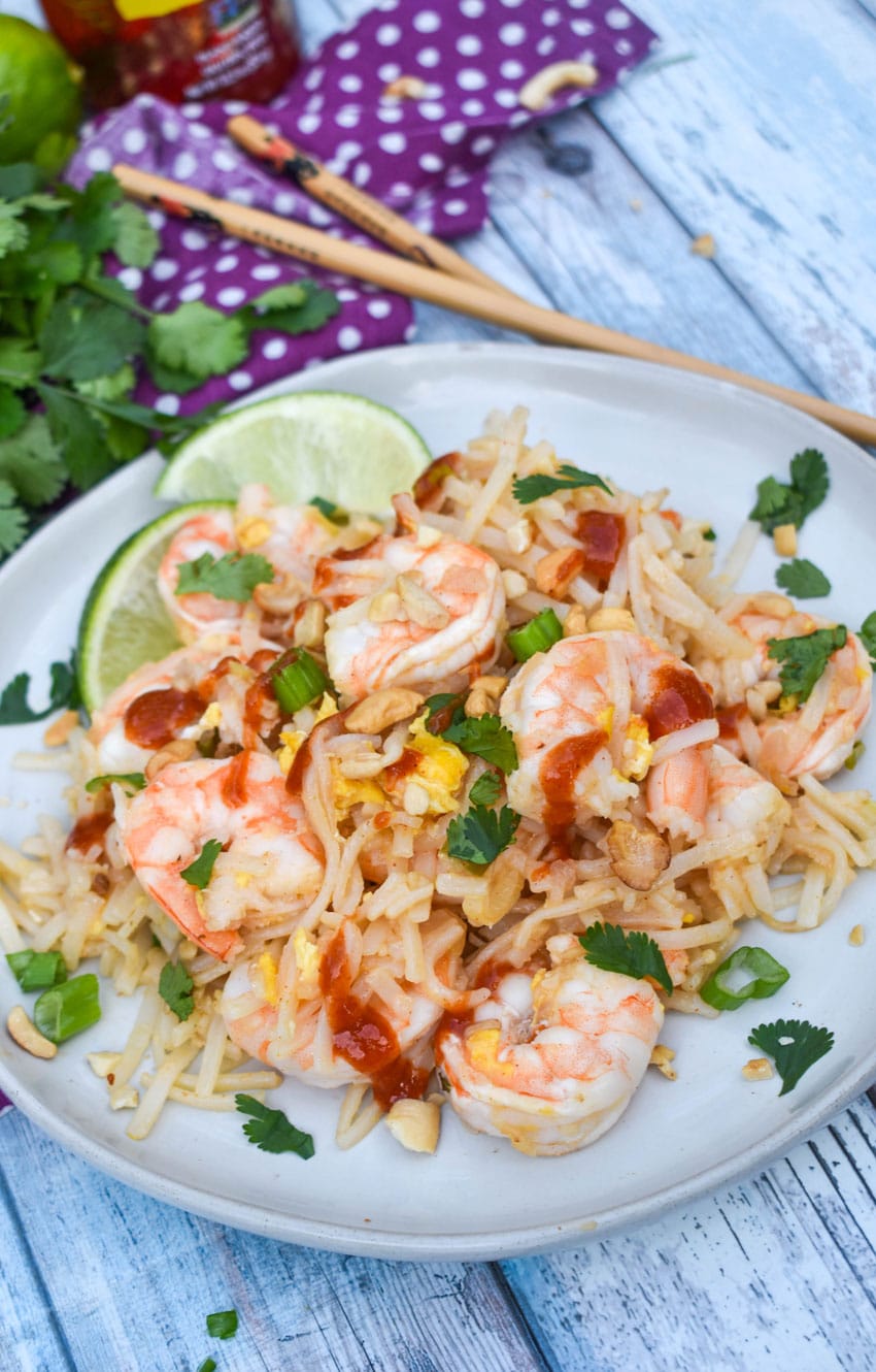 shrimp pad thai on a white plate with cilantro and chop sticks in the background