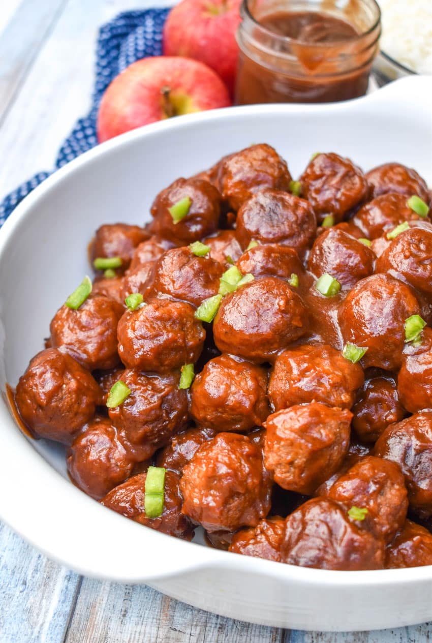 apple butter meatballs sprinkled with diced green peppers in a white serving bowl