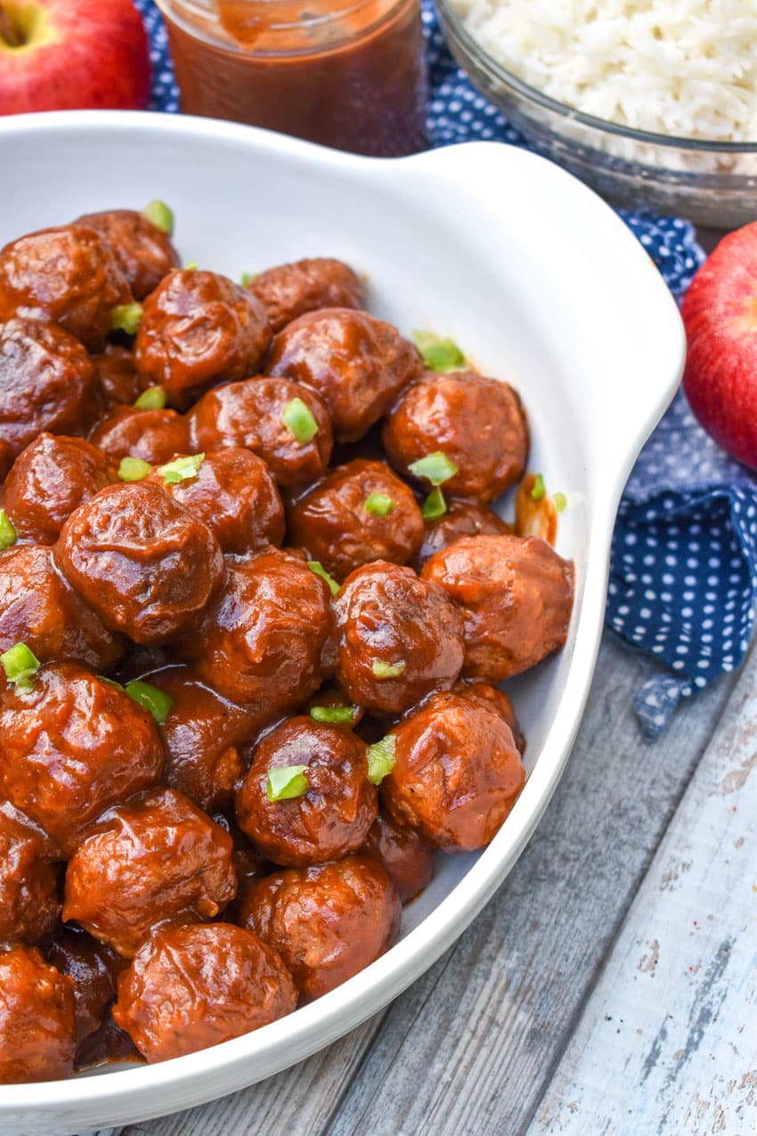 apple butter meatballs sprinkled with diced green peppers in a white serving bowl