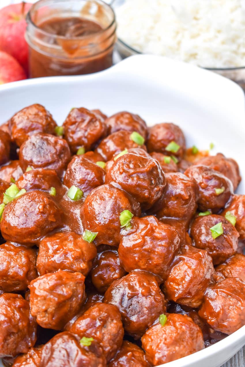 a close up of crockpot apple butter meatballs in a white serving bowl