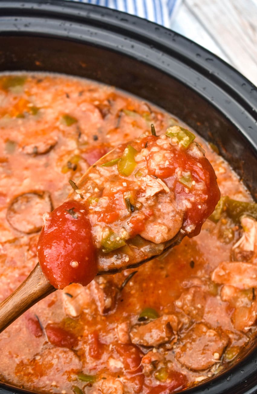 a wooden spoon scooping easy chicken gumbo out of a black crock