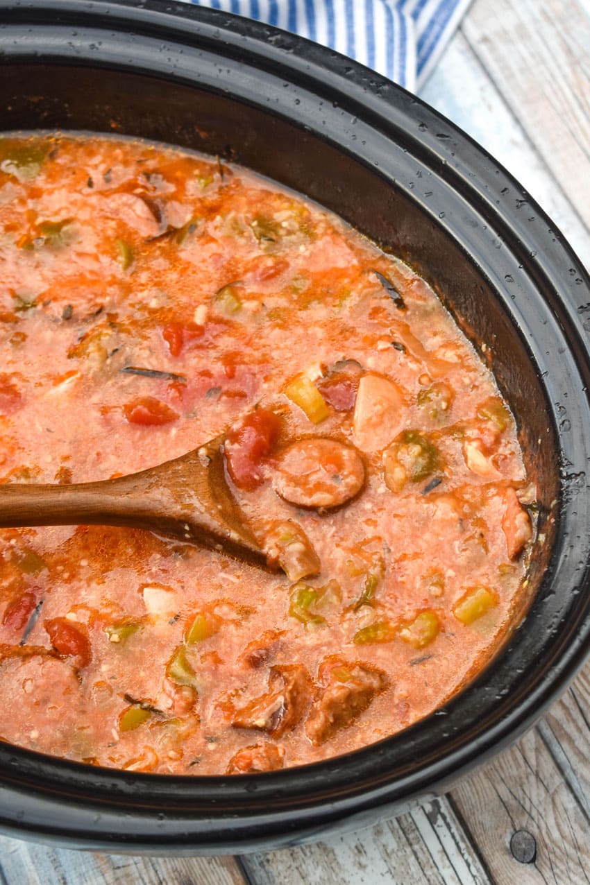 a wooden spoon scooping easy chicken gumbo out of a black crock