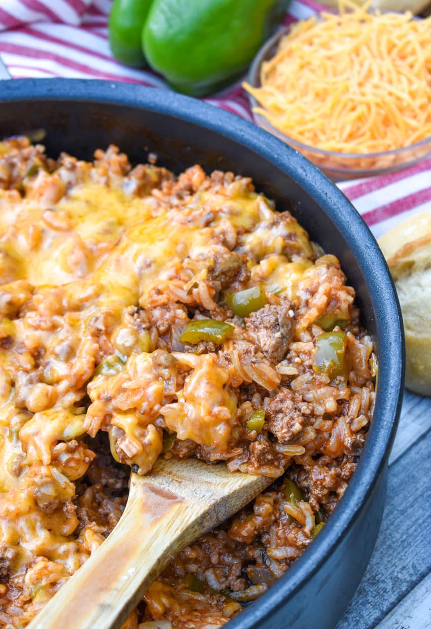 a wooden spoon scooping unstuffed pepper recipe out of a black skillet