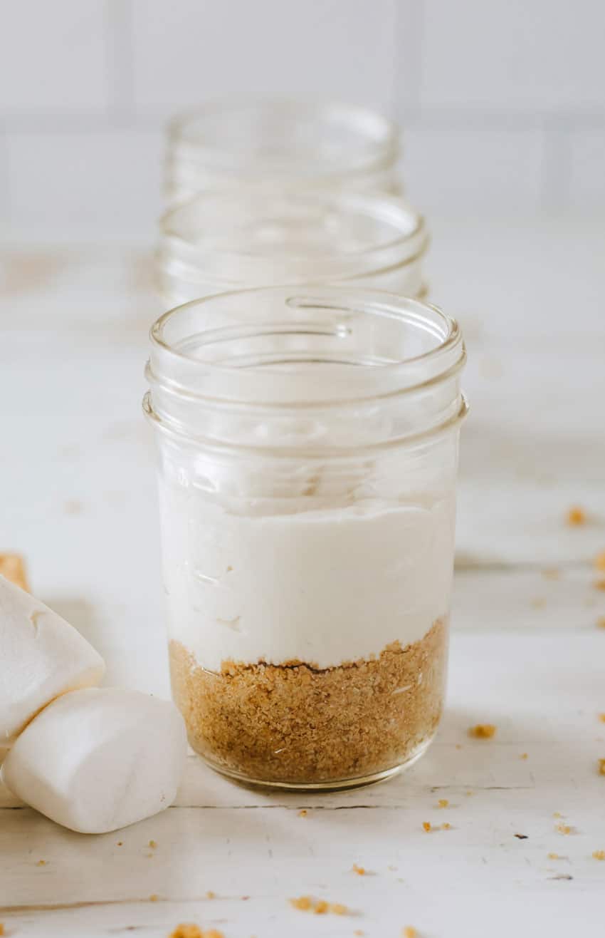 a layer of graham cracker crumbs topped with a layer of marshmallow cream cheese in a small glass jar