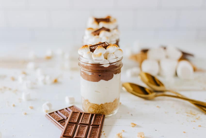 three s'mores trifles in small glass jars on a wooden table