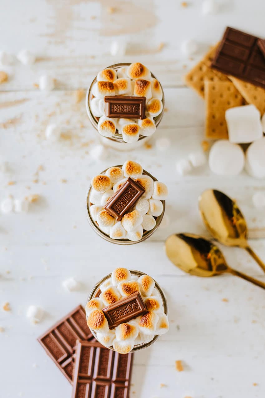 three s'mores trifles in small glass jars on a wooden table