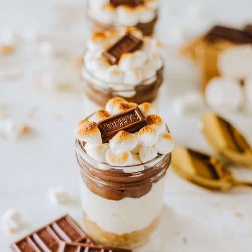 three s'mores trifles in small glass jars on a wooden table