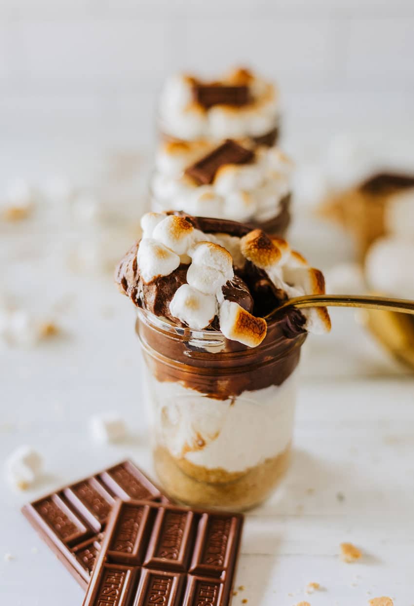 a gold spoon scooping layered s'mores trifle out of a small glass jar