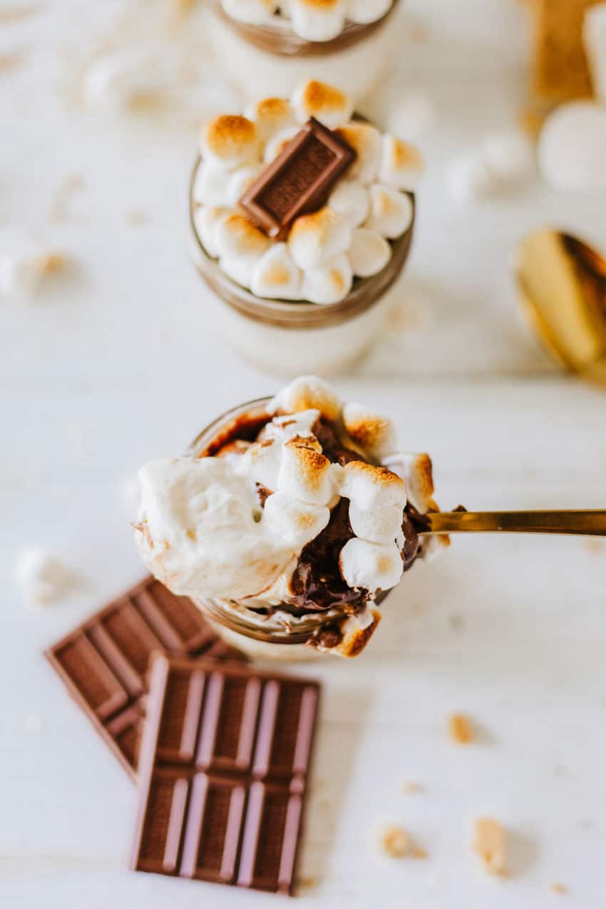 a gold spoon scooping layered s'mores trifle out of a small glass jar