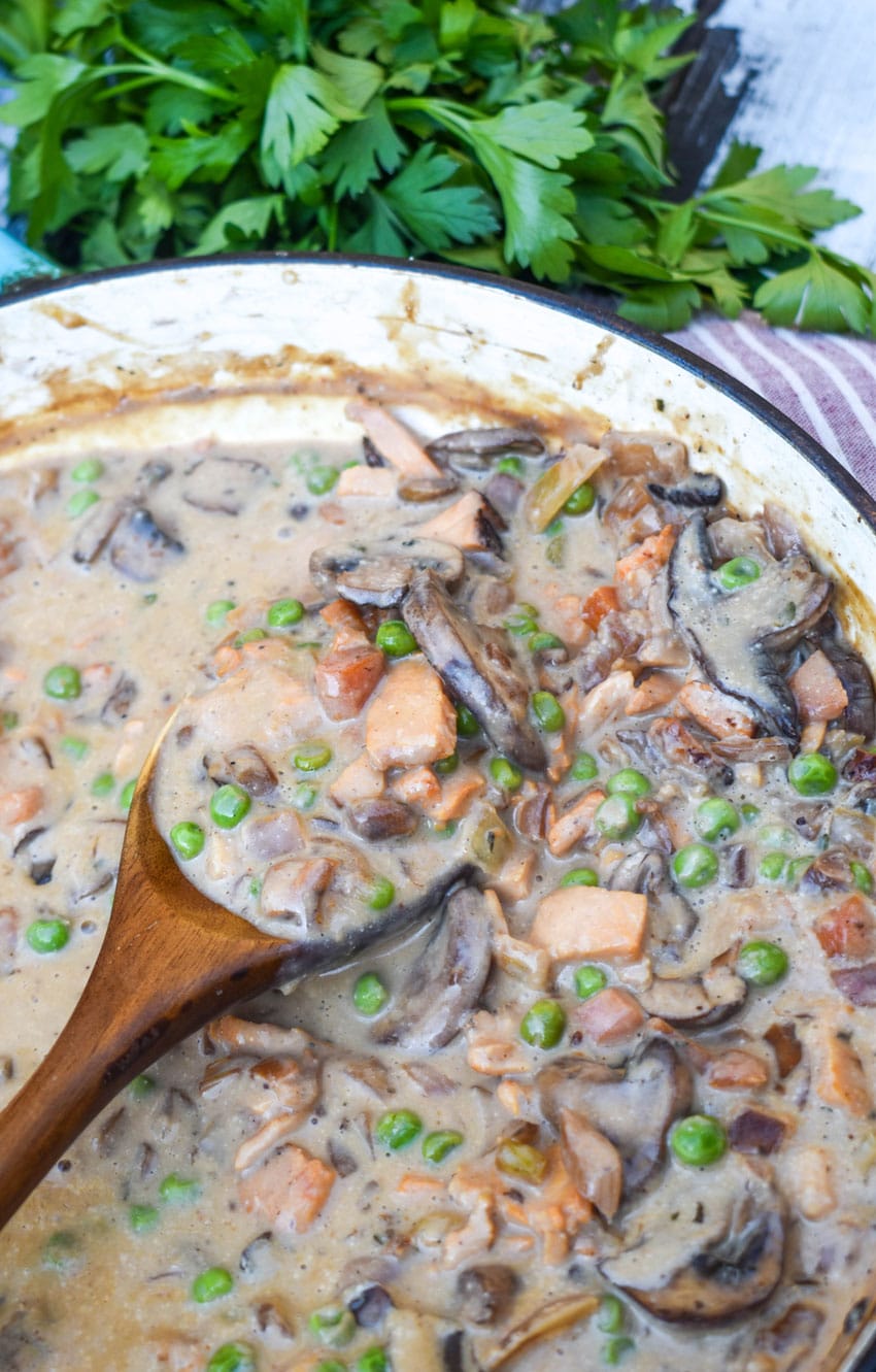 a wooden spoon scooping turkey a la king  out of a cast iron skillet