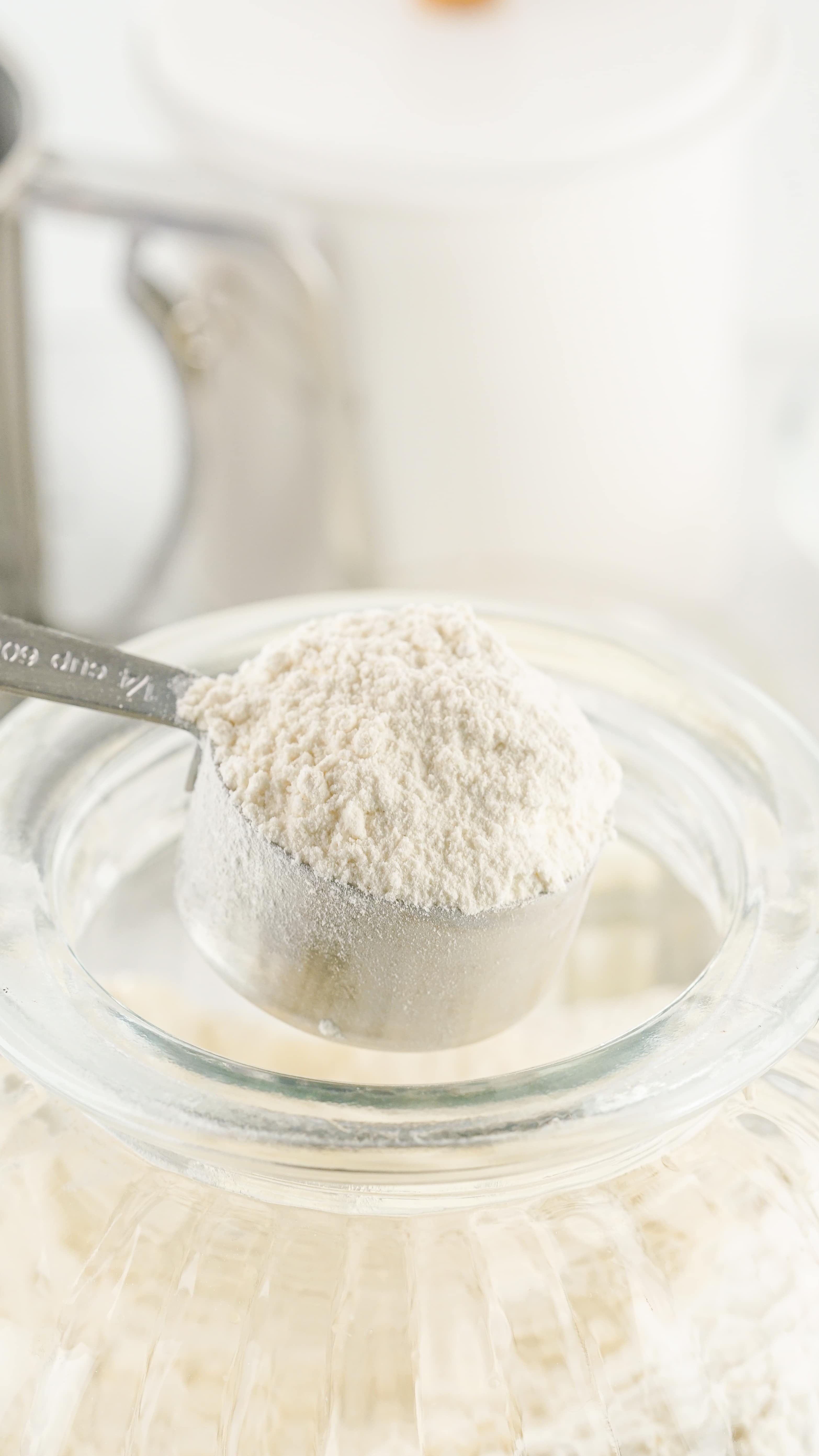 a metal measuring cup scooping homemade bisquick out of a glass jar