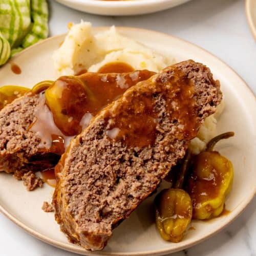 slices of mississippi meatloaf drizzled with gravy and resting against mashed potatoes on a white plate