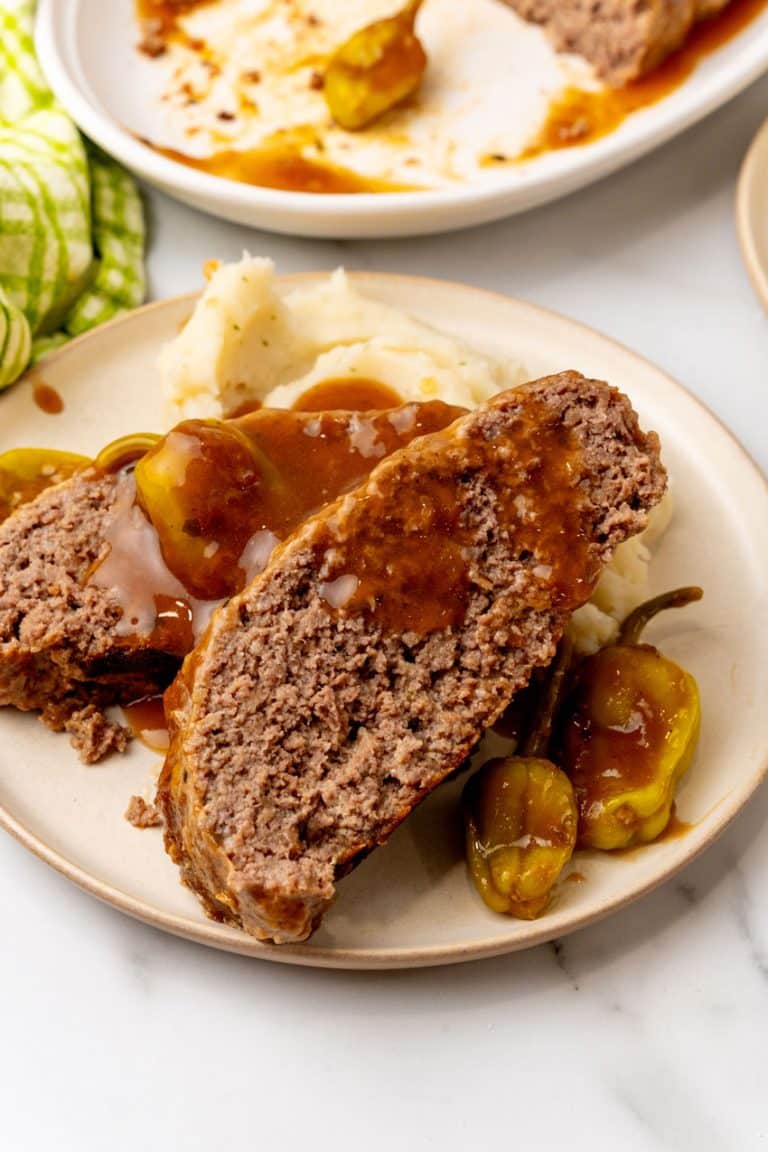 slices of mississippi meatloaf drizzled with gravy and resting against mashed potatoes on a white plate