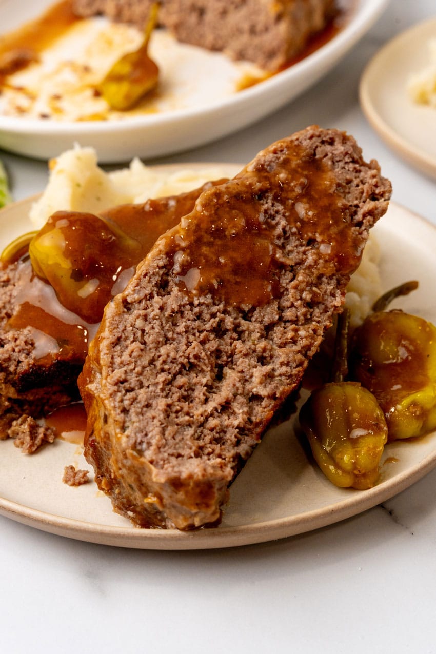 slices of mississippi meatloaf drizzled with gravy and resting against mashed potatoes on a white plate