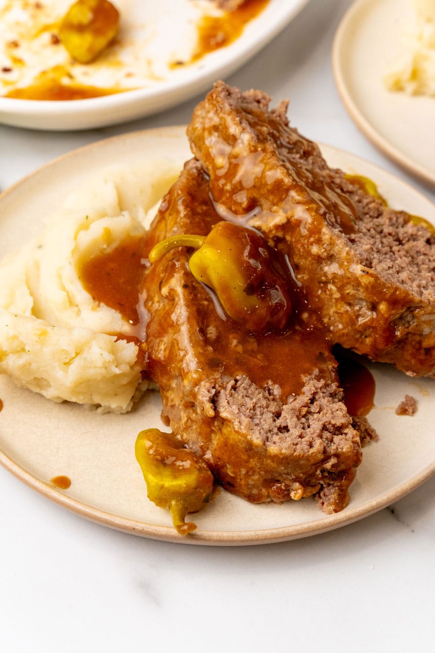 slices of mississippi meatloaf drizzled with gravy and resting against mashed potatoes on a white plate