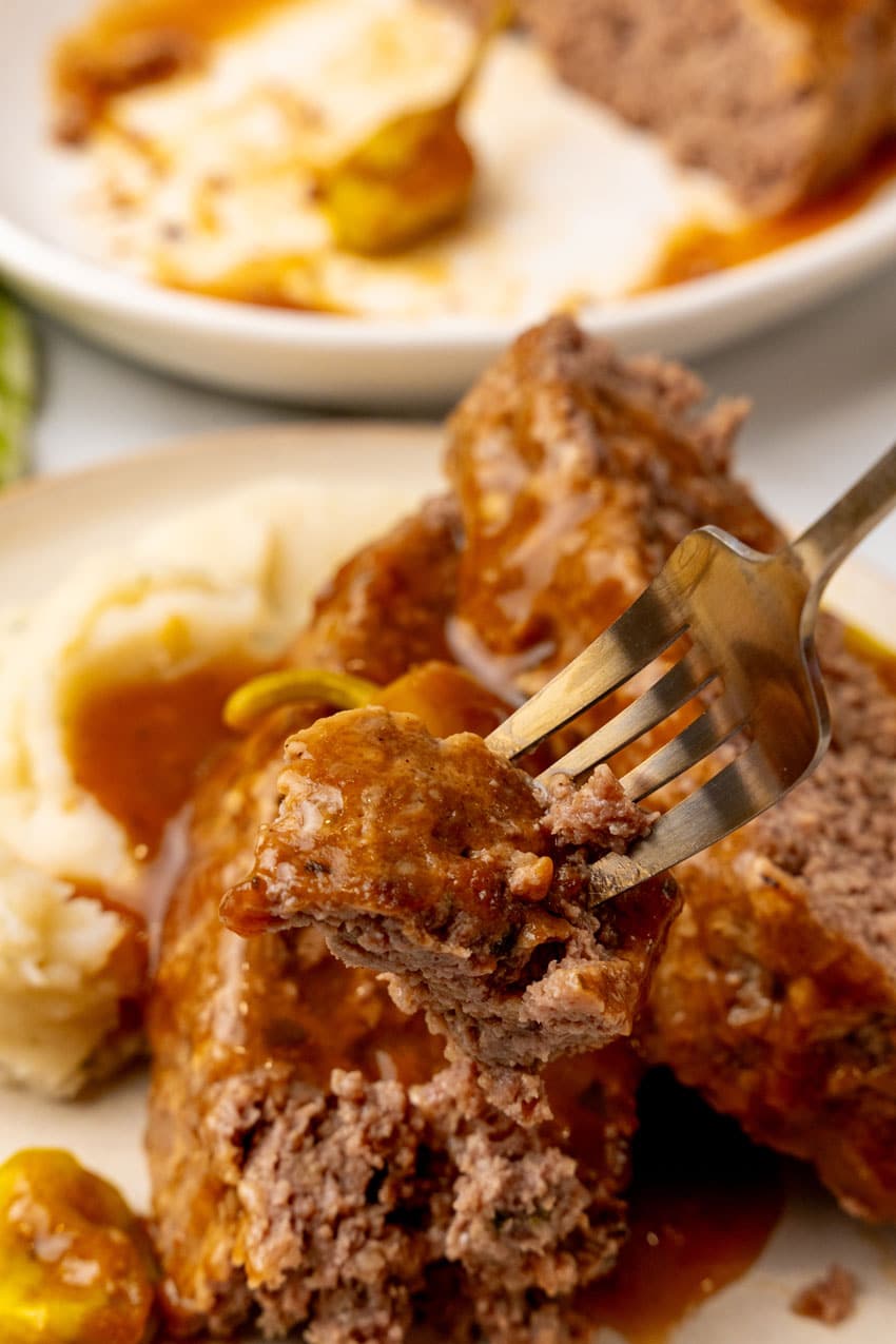 a silver fork holding up a piece of mississippi meatloaf with gravy