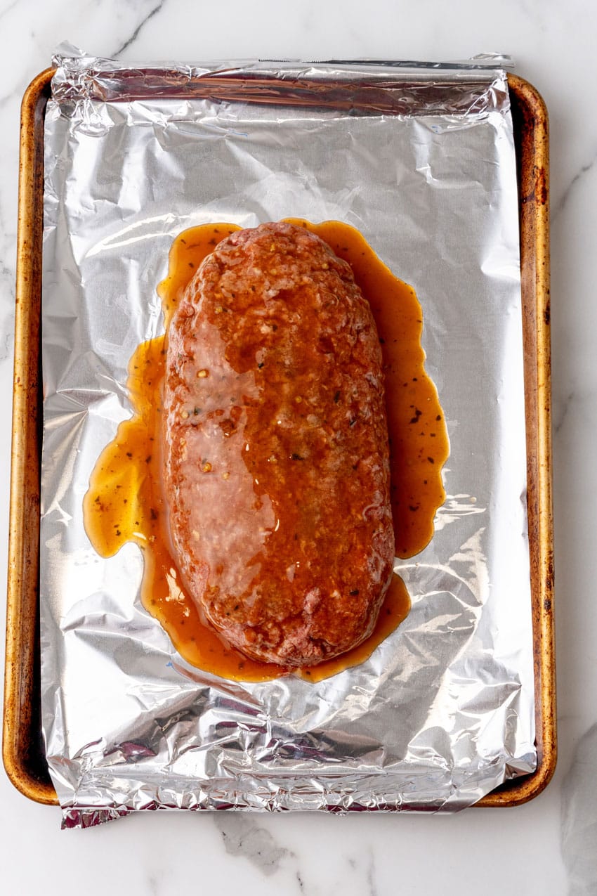 unbaked meatloaf covered in brown gravy resting in the center of a foil lined baking sheet