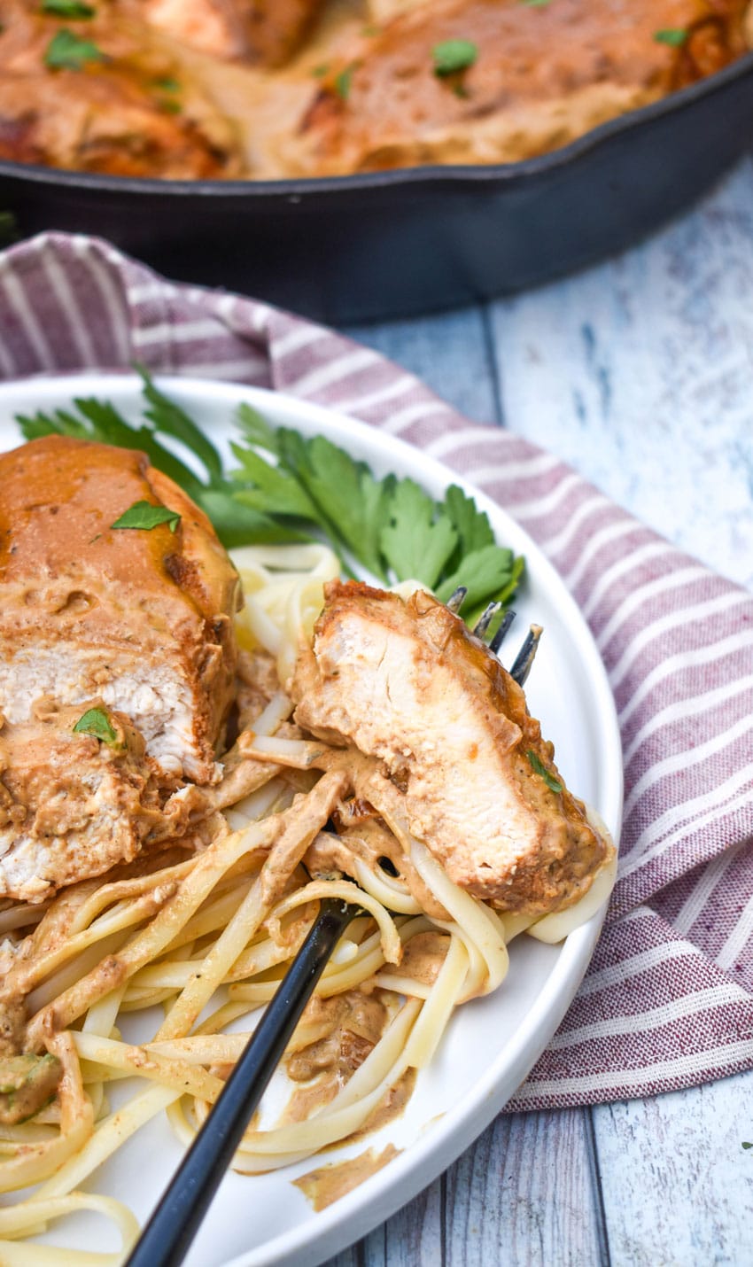 a sliced piece of boursin chicken in cream sauce over cooked pasta on a white plate with fresh herbs on the side