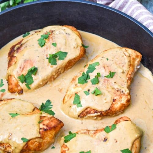 four pieces of boursin chicken in cream sauce topped with fresh herbs in a large cast iron skillet