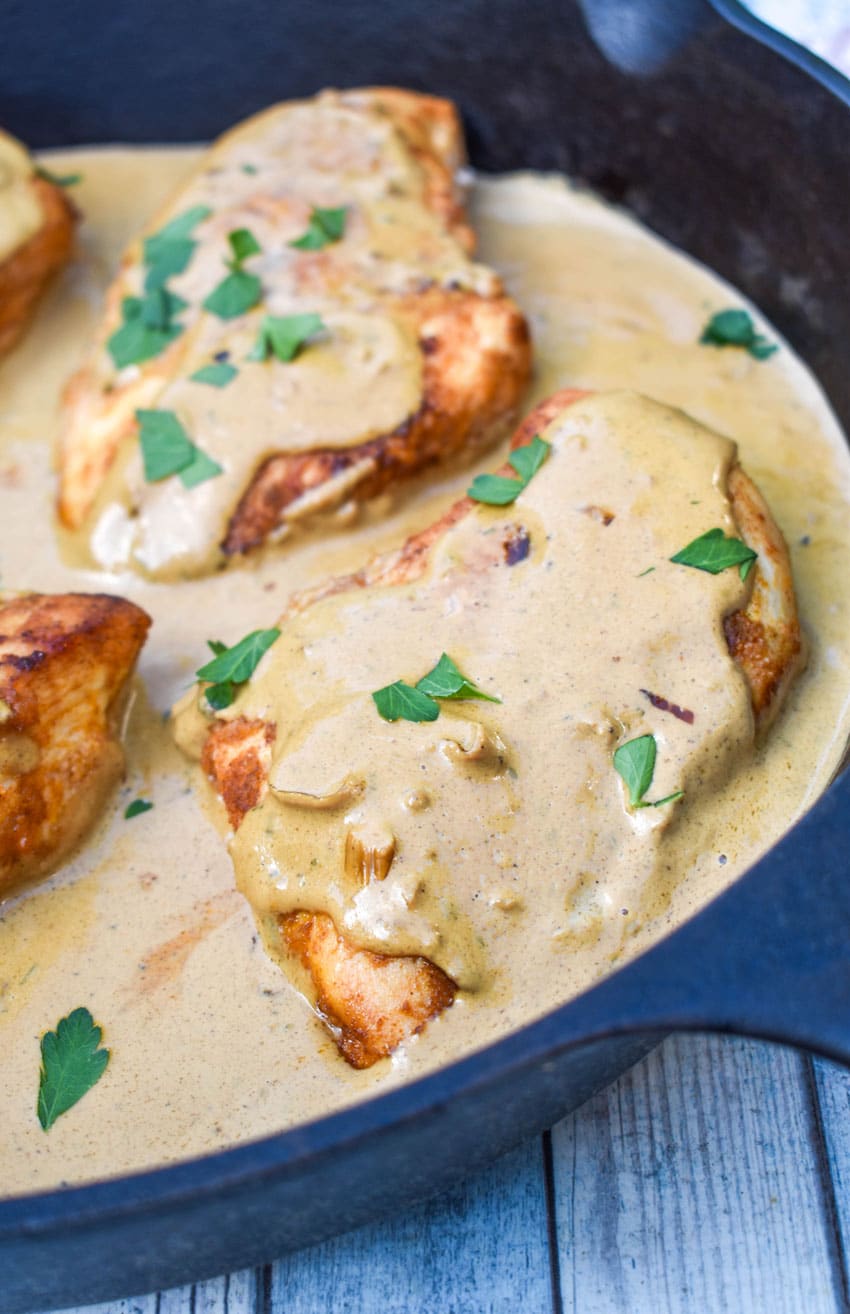 four pieces of boursin chicken in cream sauce topped with fresh herbs in a large cast iron skillet