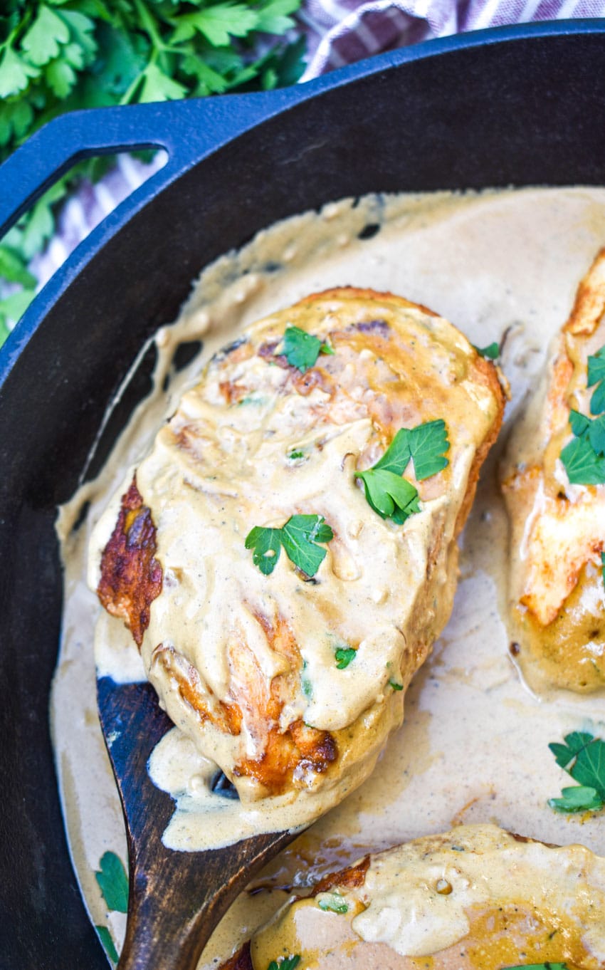 a wooden spatula scooping a piece of boursin chicken in cream sauce out of a cast iron skillet