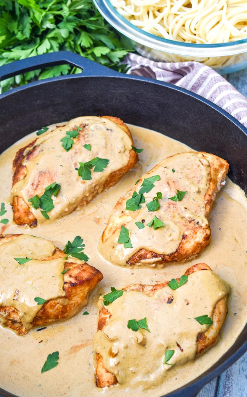 four pieces of boursin chicken in cream sauce topped with fresh herbs in a large cast iron skillet