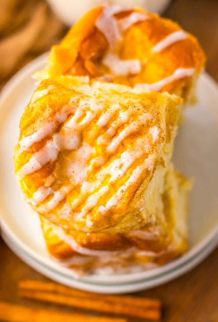 two pumpkin danish hawaiian rolls stacked on a small white dessert plate