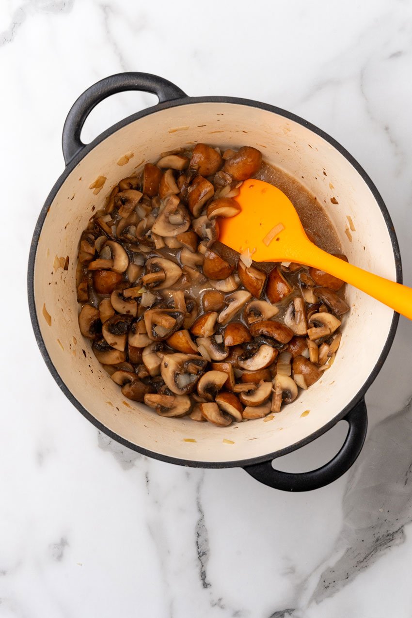 mushrooms and onions sauteeing in butter in a large dutch oven