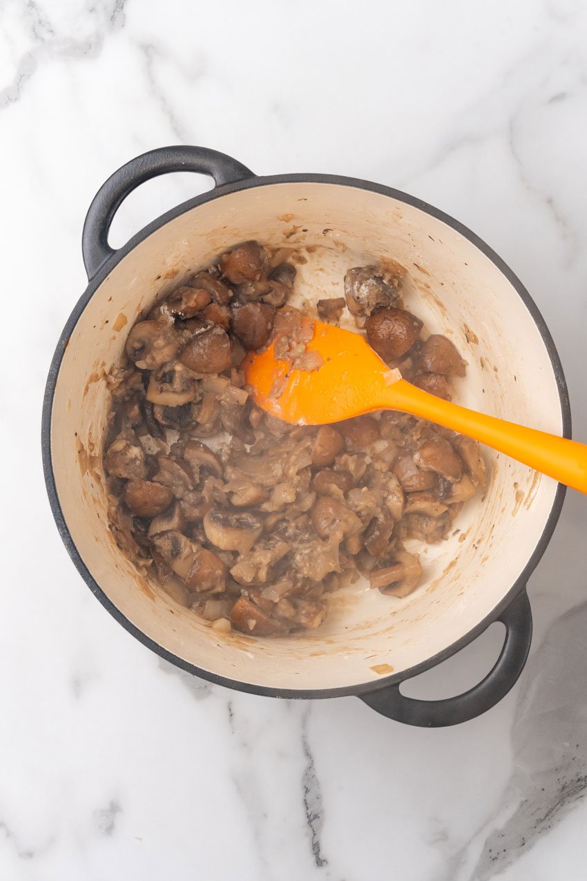 mushrooms and onions sauteeing in butter in a large dutch oven